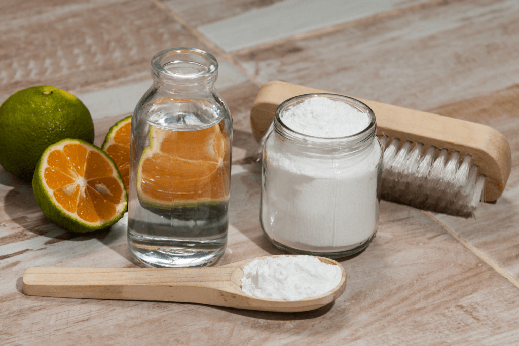a wooden spoon with a jar of white powder and a glass jar of water next to a brush and a couple of oranges