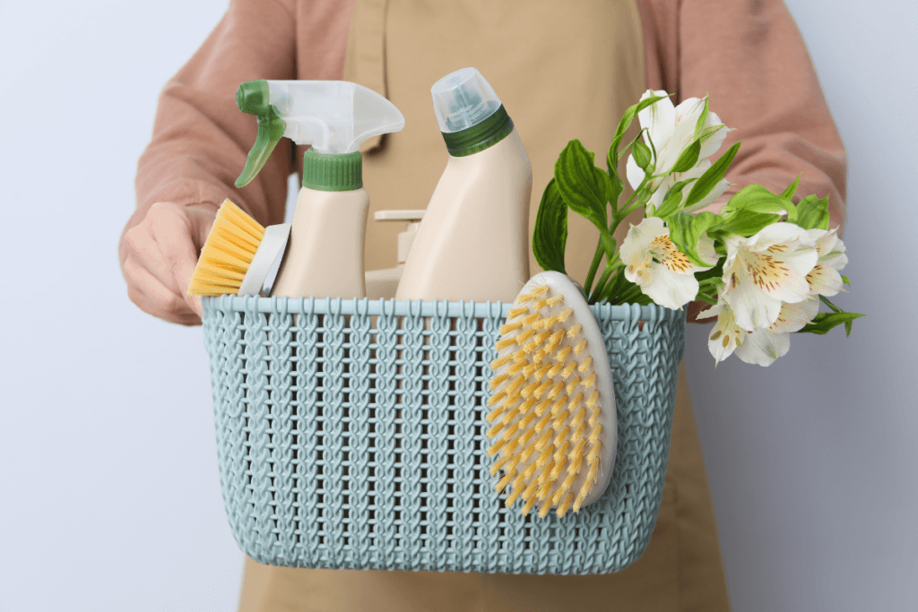 a person holding a basket with cleaning supplies and flowers