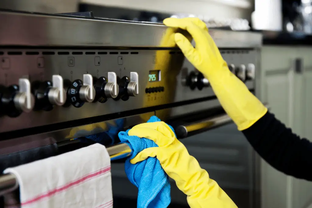 a person wearing yellow gloves cleaning a stove