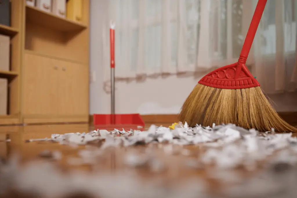 a broom and a pile of shredded paper on a wooden floor