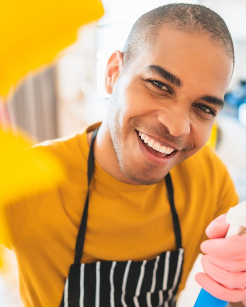 a man wearing a black apron and gloves holding a spray bottle